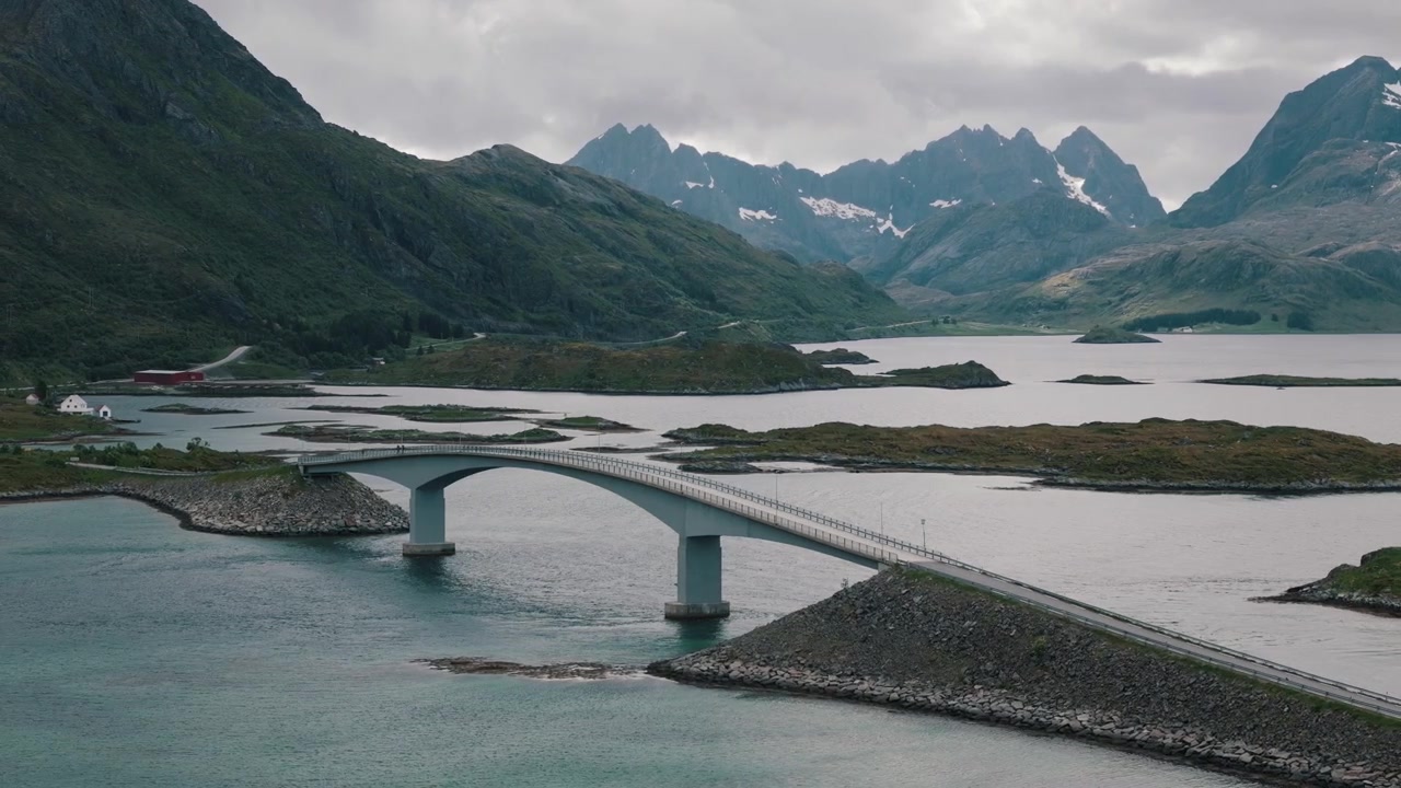 Folk krydser Flakstad Bro under tårnhøje Lofoten-bjerge.
