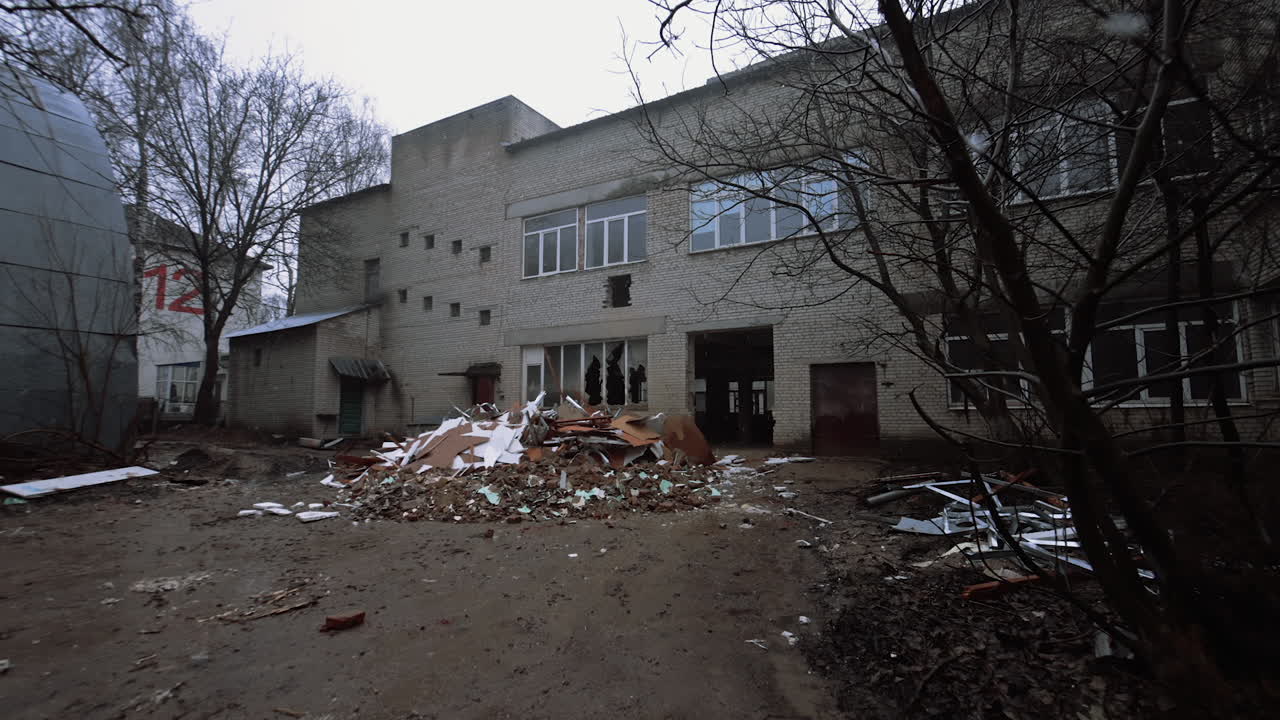 Coming closer to an old building with big windows, one of which is broken. Huge piles of debris are in front of the premise.