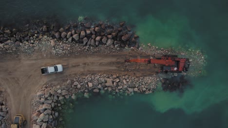 Schwere-Maschinen-Rechtzeitig-Auf-Dem-Wellenbrecher,-Hitachi-Zaxis-Mit-Großer-Reichweite,-Fahrzeug-Und-LKW-Mit-Großen-Steinen,-Ansicht-Von-Oben-Nach-Unten