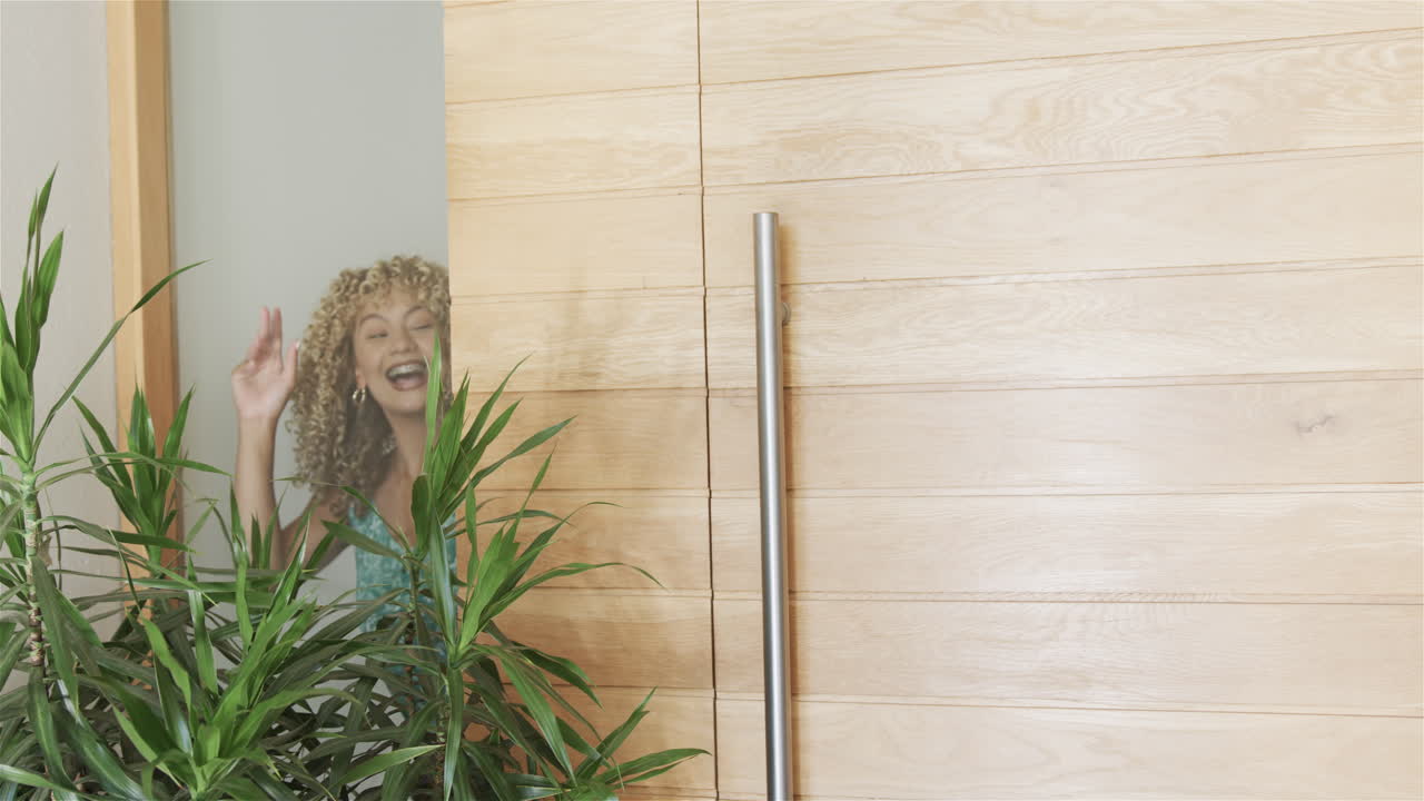 joven biracial abriendo su puerta principal y saludando, con espacio de copia