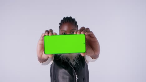 a woman holding her green screen smartphone directly towards the camera in studio and doing various hands movement with it.