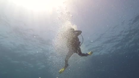 Girl-Scuba-Diving-in-blue-sea-of-the-Atlantic-Ocean,-with-the-sun-above