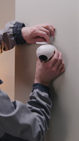 man installing a white security camera on a wall