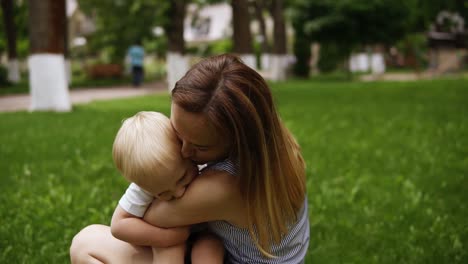 Fröhlicher,-Lächelnder-Blonder-Junge,-Der-Glücklich-Rennt-Und-Seiner-Mutter-Die-Zunge-Herausstreckt.-Freudige-Momente.-Mutter-Umarmt-Und-Küsst-Ihr-Kind.-Grüner-Park