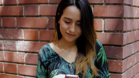 Woman-leaning-on-a-brick-wall-using-a-mobile