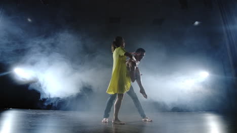 una pareja está bailando rápido y haciendo trucos acrobáticos en cámara lenta en el escenario en el humo y los reflectores