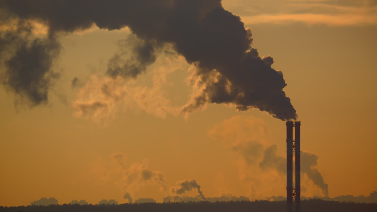 Fumaioli industriali che rilasciano fumo scuro nel cielo al tramonto. Inquinamento atmosferico, emissioni di fabbrica, problema ambientale, industria, drammatica luce serale e movimento del fumo che trasmettono problemi ambientali