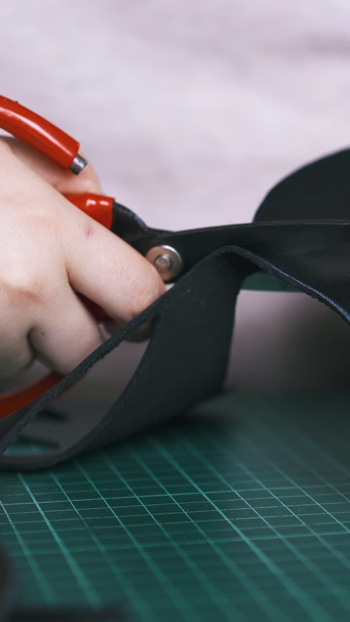 CU: Skilled designer cuts black leather cloth making mask with special scissors on cushion board closeup