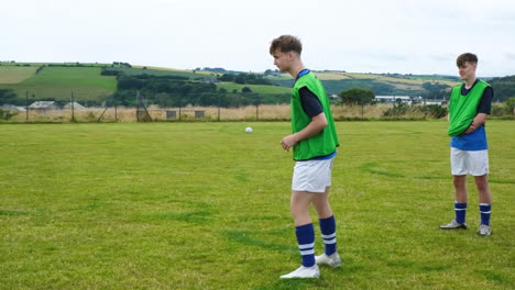 soccer player kicking ball on grassy field near scenic lake and hills