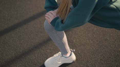 close up of lady in white canvas sneakers stretching with hand on knee, focusing on athletic posture and movement, showcasing healthy lifestyle in outdoor workout environment with shadow