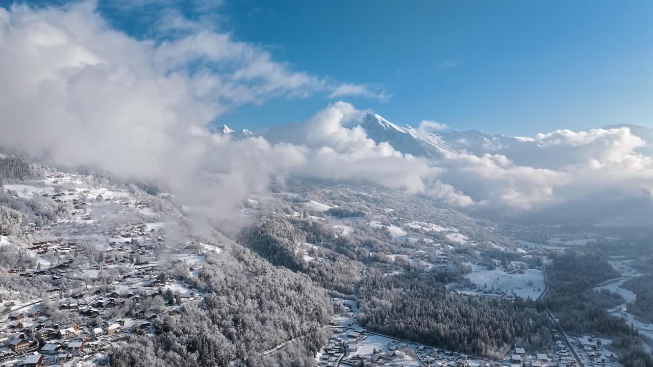 Sneklædt luftfoto af Giffre-dalen med bjerge, skyer og en vinterlandsby