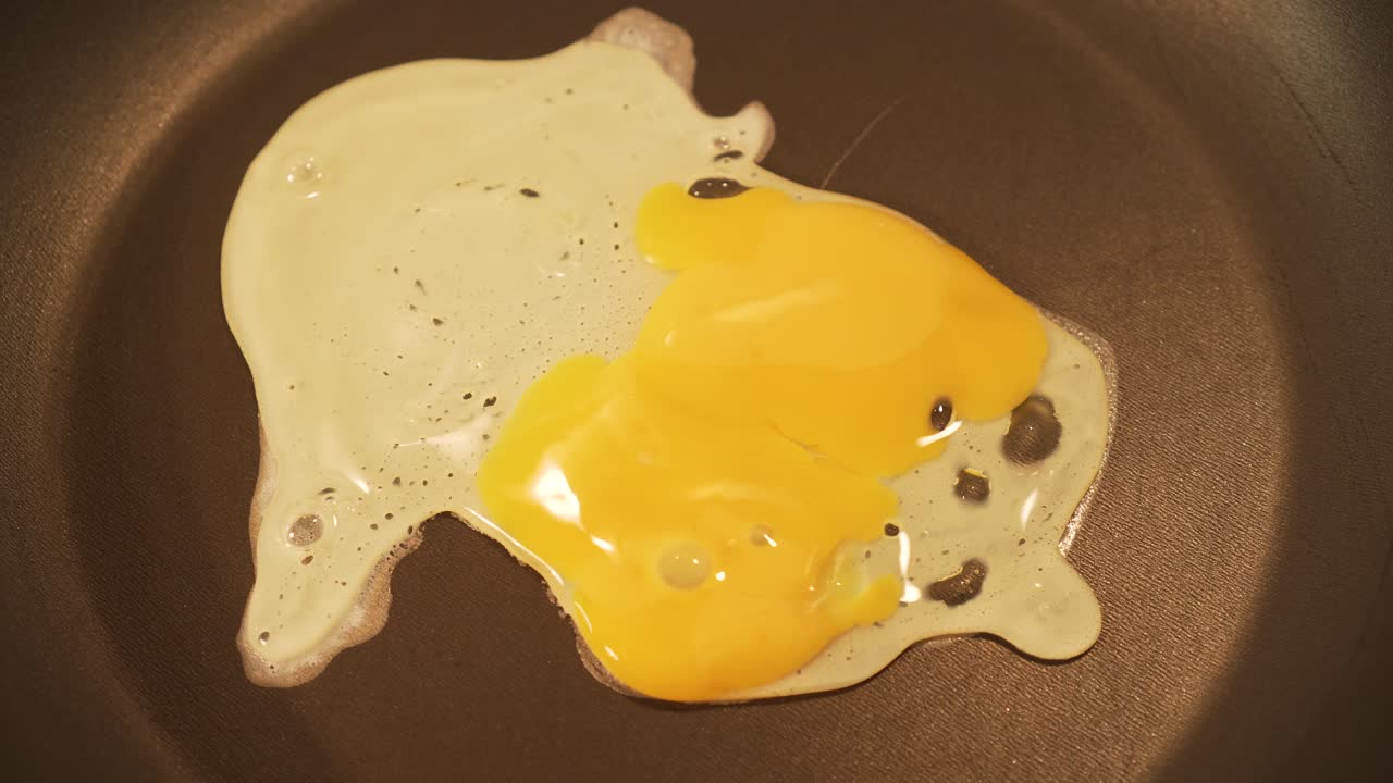 Ei fällt in die Pfanne, das Eigelb wechselt die Farbe von Gelb zu Weiß – Nahaufnahme.