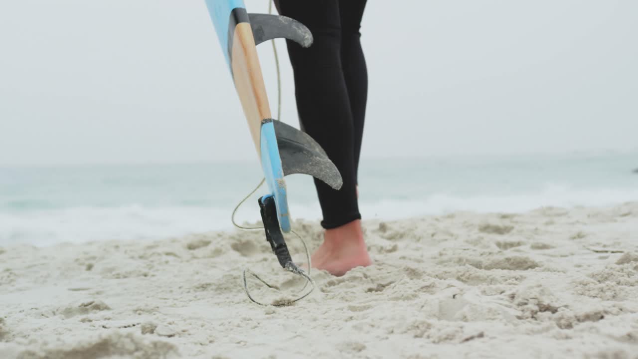 Low section of male surfer walking with surfboard on the beach 4k