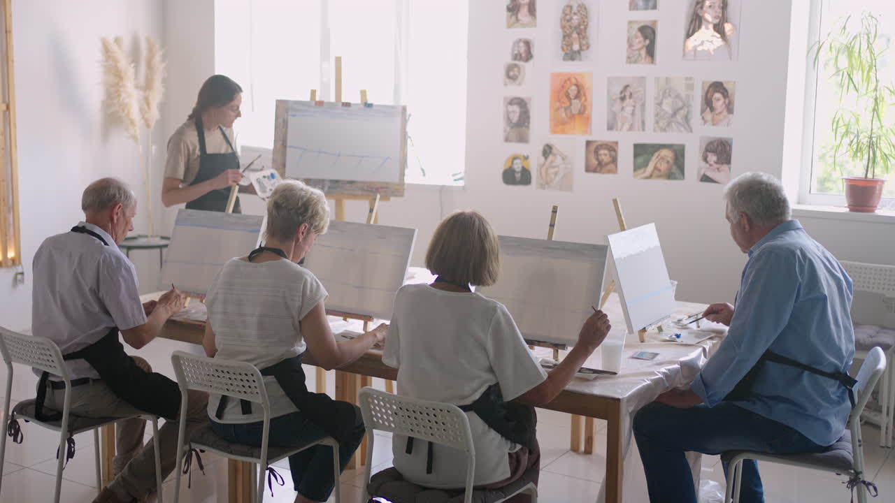 учитель показывает группу друзей пенсионеров на курсах рисования. группа пожилых мужчин и женщин рисуют вместе и улыбаются