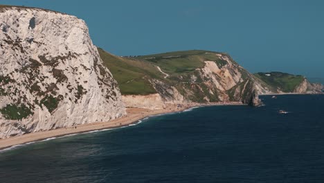 slow approach drone flight toward durdle door with sea waves and beach unfolding ahead, establishing aerial