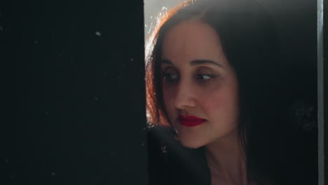 intense close-up of a woman's face with striking red lips, framed against a dark, softly lit background, capturing a moment of deep expression