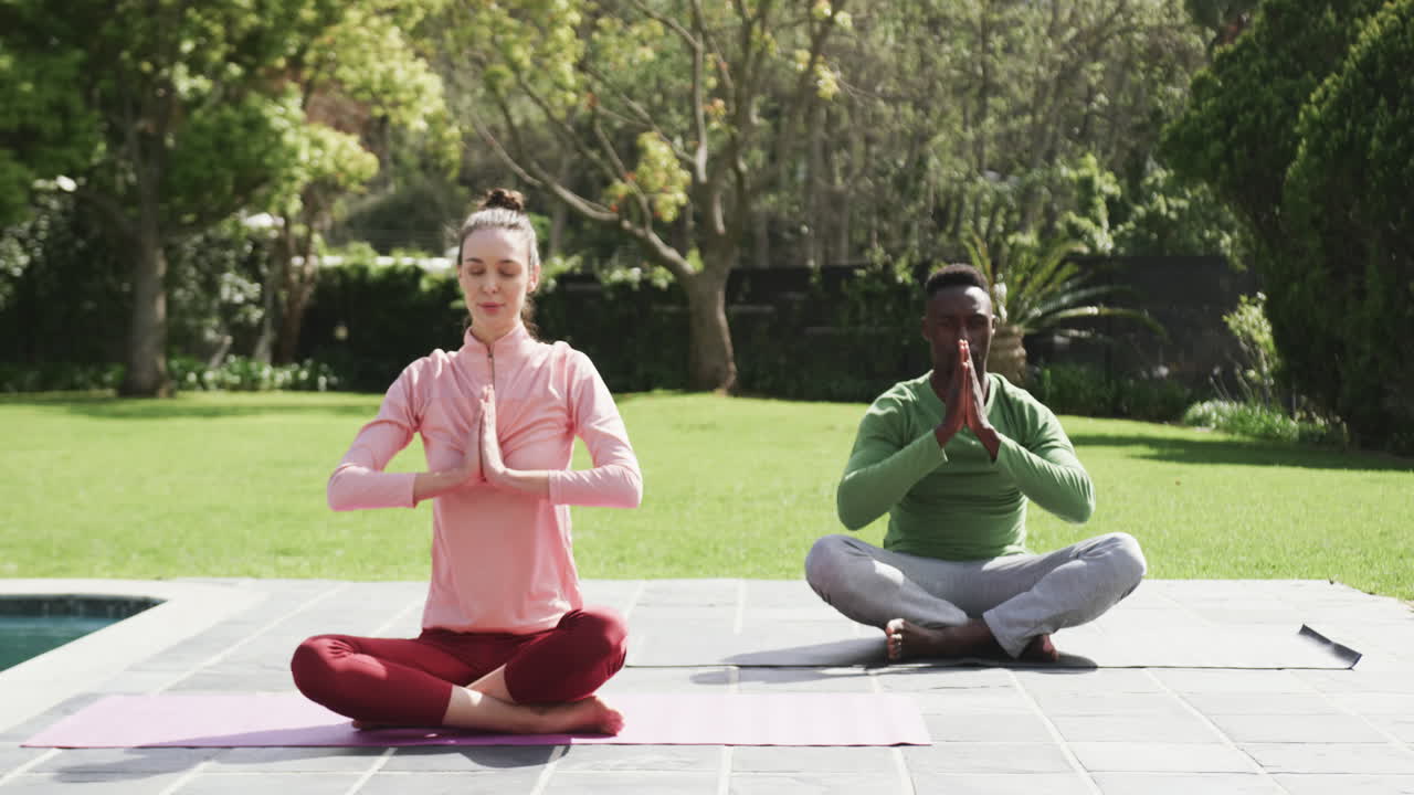 una pareja feliz y diversa haciendo yoga en un jardín soleado, en cámara lenta.