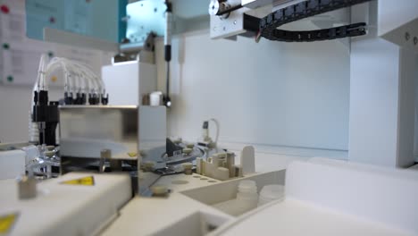 primer plano de una aguja de laboratorio larga y afilada que se mueve rápidamente en un analizador moderno que mueve y pipeta muestras de sangre en una pequeña clínica médica
