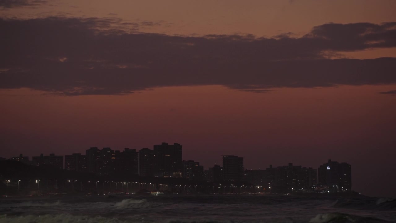 Ligne d'horizon en silhouette d'une ville côtière au crépuscule – Vagues au premier plan.