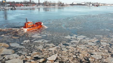 Aerial-view-follows-small-red-ship-sailing-along-drifting-ice-floes