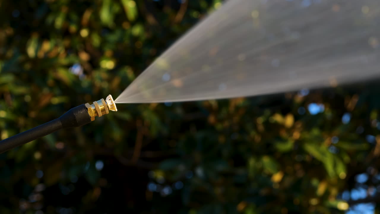 Power washer with white tip sprays high powered water jet with trees in background