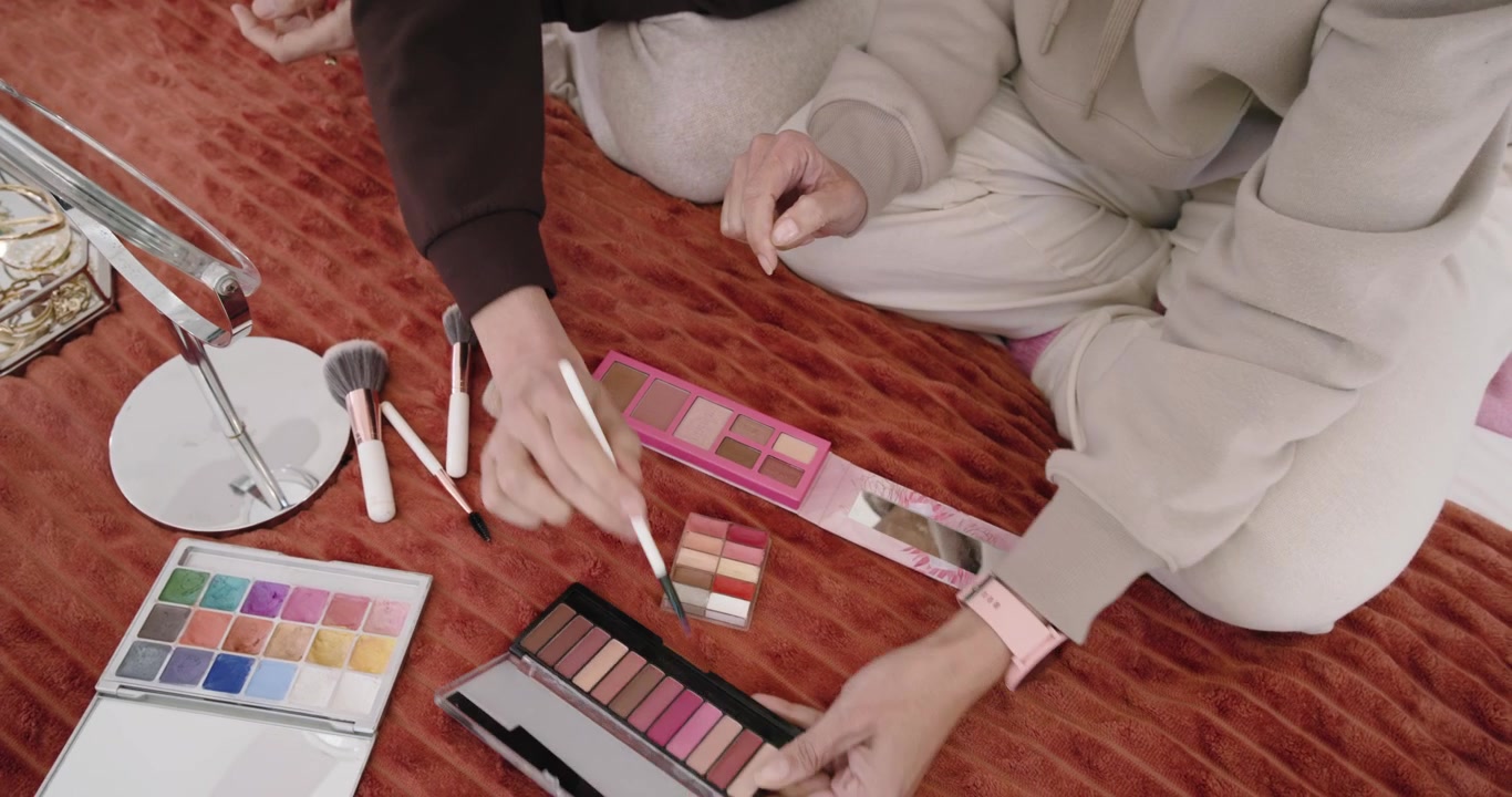 Aprendo una palette rosa su una trapunta, gli amici intingono i pennelli, testando le tonalità sui polsi per abbinare i colori.