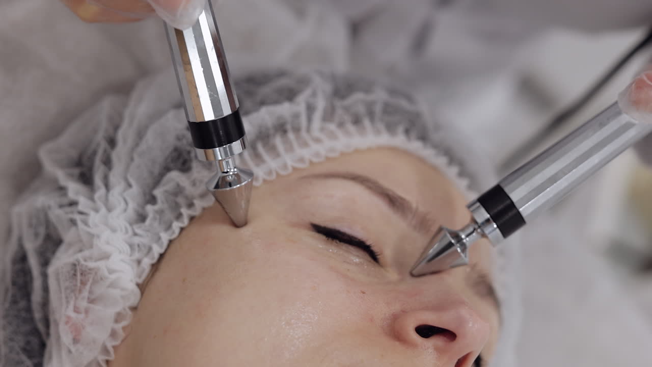 Beautician doctor makes woman micro currents face therapy using electrical impulses in spa salon