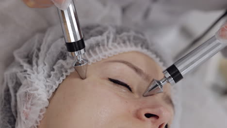 la doctora esteticista hace a la mujer micro corrientes terapia facial usando impulsos eléctricos en el salón de spa