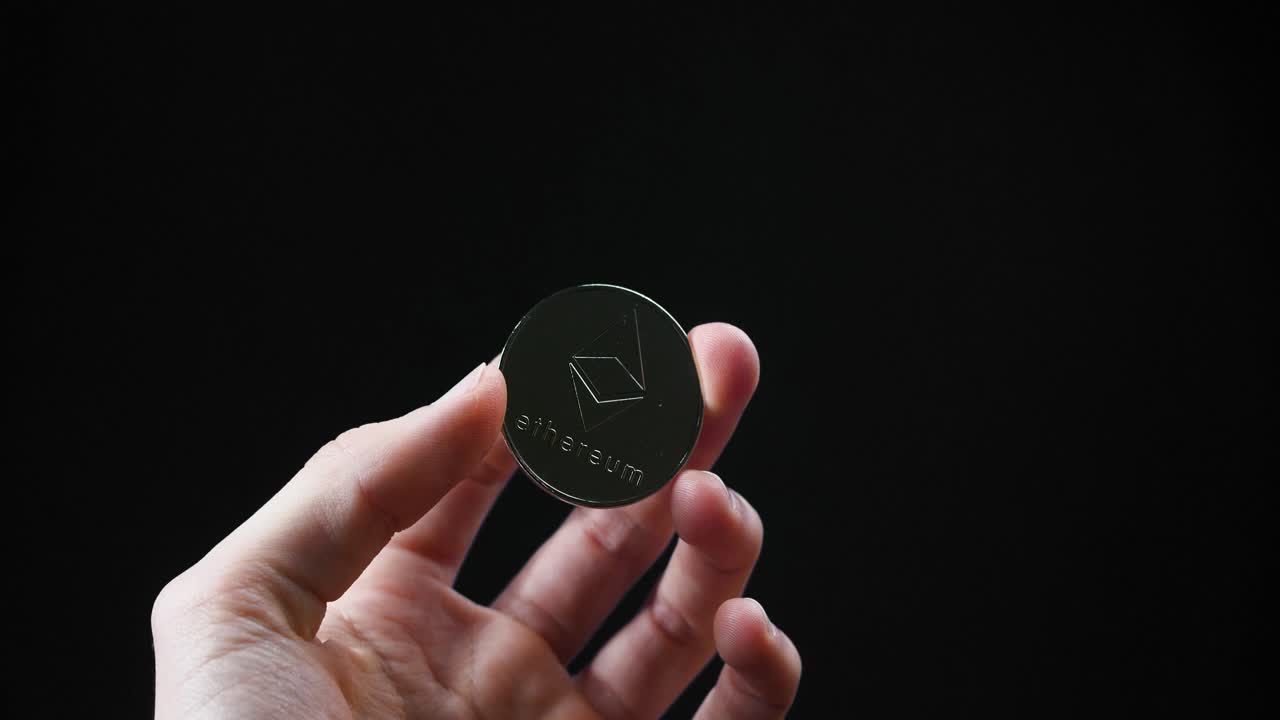 A close-up of a hand holding a single Ethereum coin shining against a black backdrop