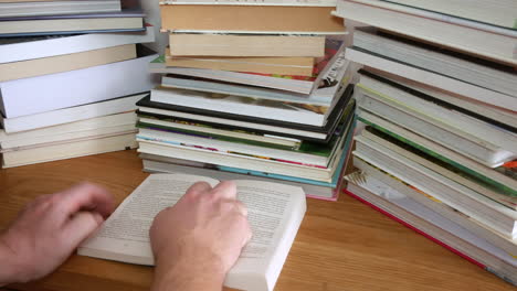 un hombre irreconocible está leyendo un libro con montones de libros en el escritorio