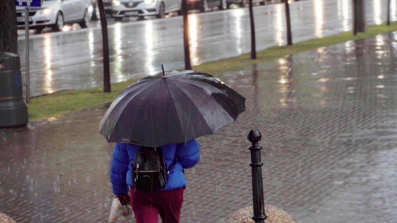 Femme traversant la rue sous la pluie avec un parapluie noir