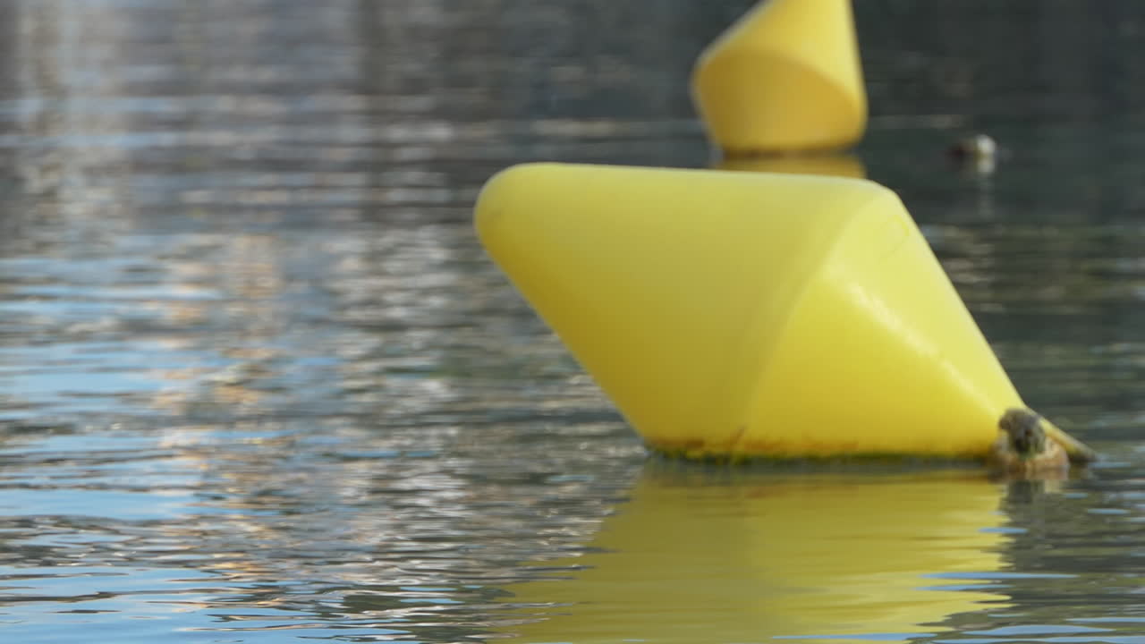 Close-up of a yellow navigation buoy moving slowly in clear water with its mirror reflection visible.