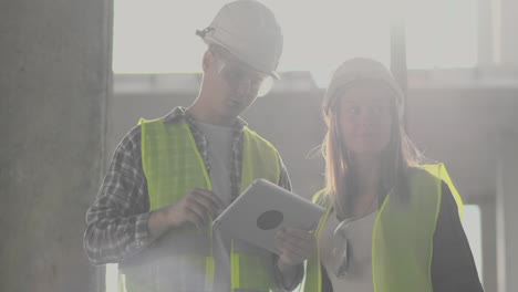 Un-Trabajador-De-La-Construcción-Y-Una-Arquitecta-Con-Casco-Discuten-El-Plan-De-Construcción-De-La-Casa-Y-Se-Cuentan-Sobre-El-Diseño-Sosteniendo-Una-Tableta,-Miran-El-Fondo-De-Los-Dibujos-De-Los-Rayos-Del-Sol.