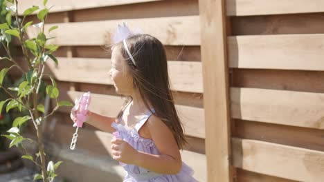 a little girl in a dress is blowing soap bubbles in the backyard on a sunny summer day