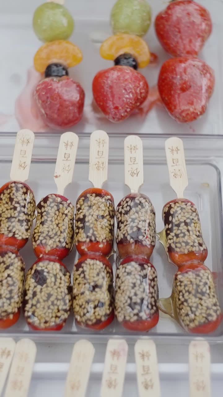 Close up view of fresh and delicious asian japanese sweets called tanghulu, made with sugar coated tangerines, grapes and strawberries in a street food market.