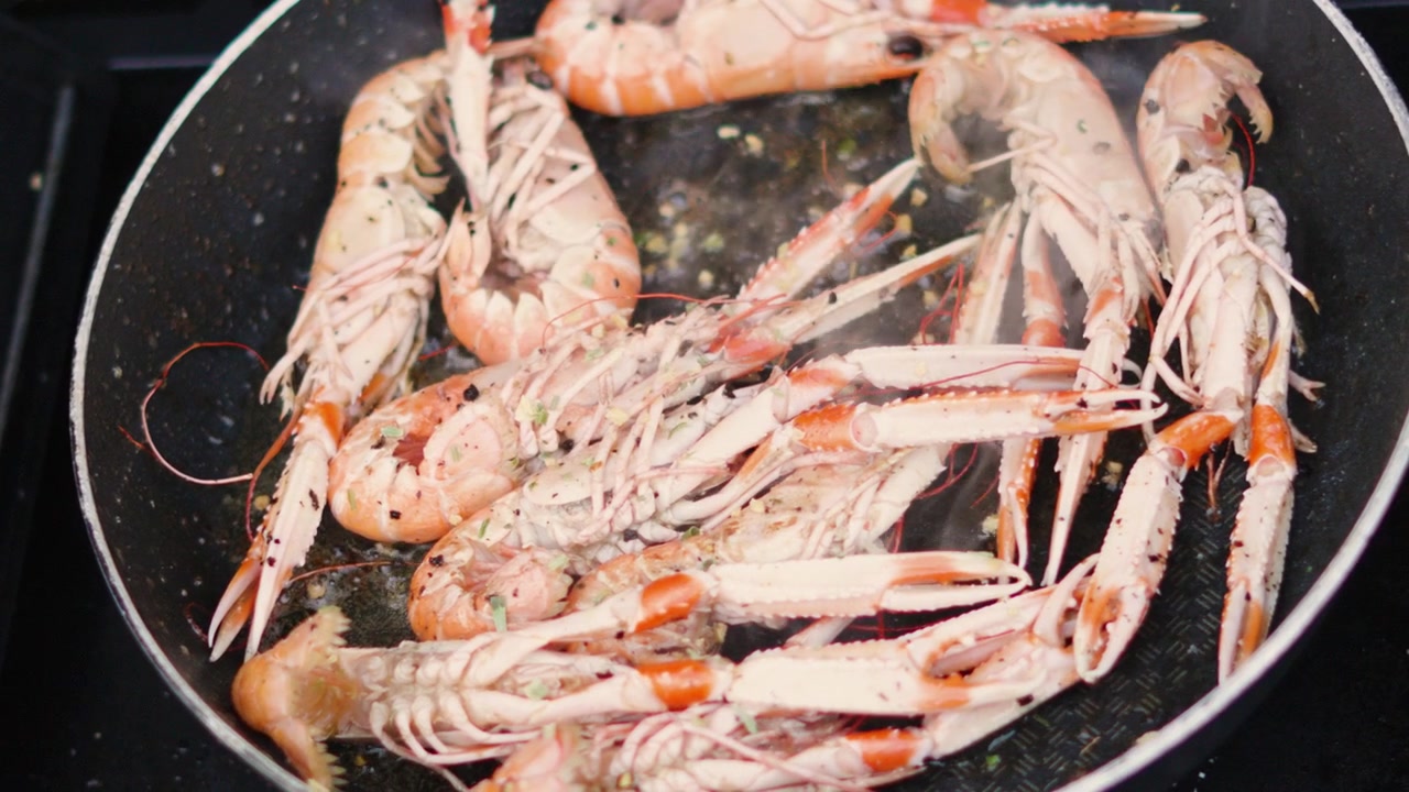 Vista dall'alto di aglio fresco che cade su scampi freschi che cuociono in una padella calda. Frutti di mare cotti all'aperto al rallentatore. Scampo norvegese.