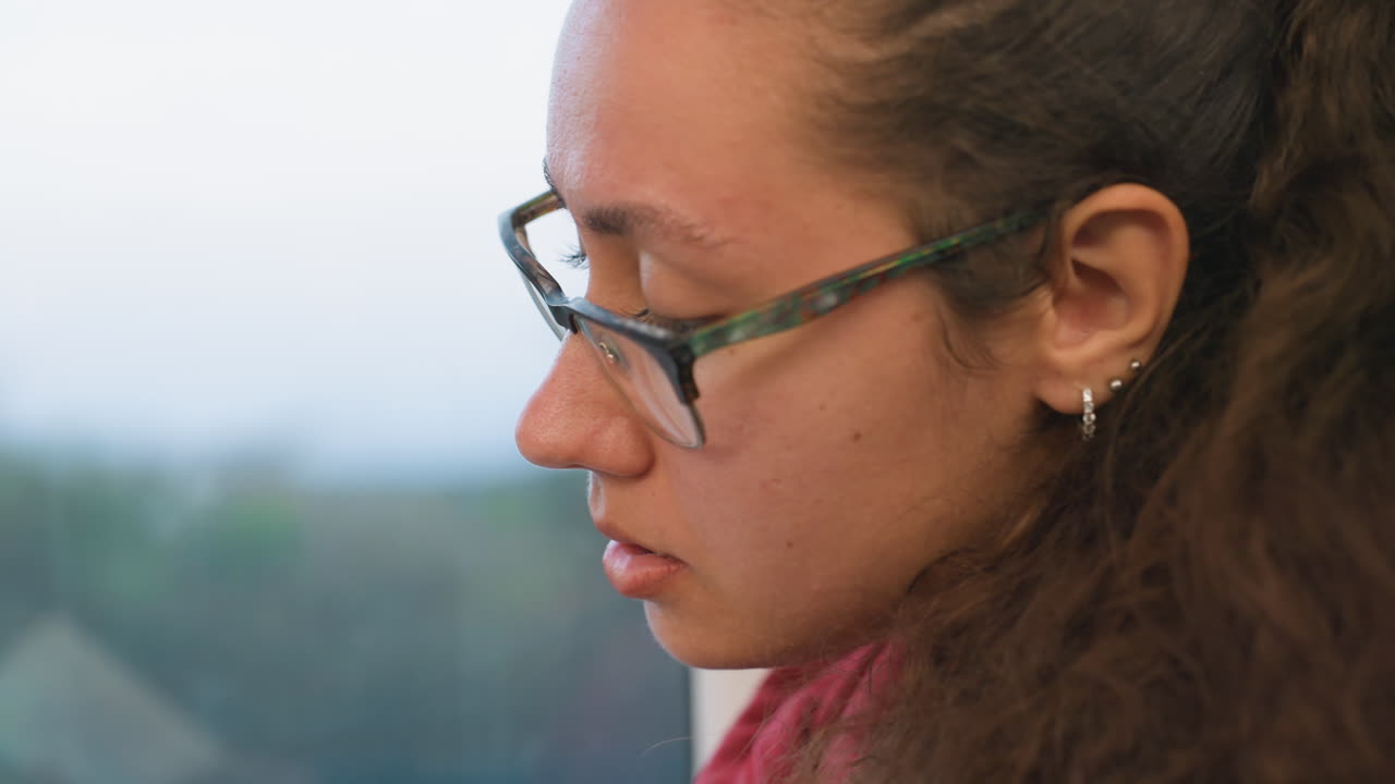 Una donna guarda attraverso il finestrino del treno. Ragazza con gli occhiali osserva la campagna che scorre dolcemente attraverso il finestrino. Giovane donna con gli occhiali osserva delicatamente il paesaggio pittoresco che scorre fuori dal treno.