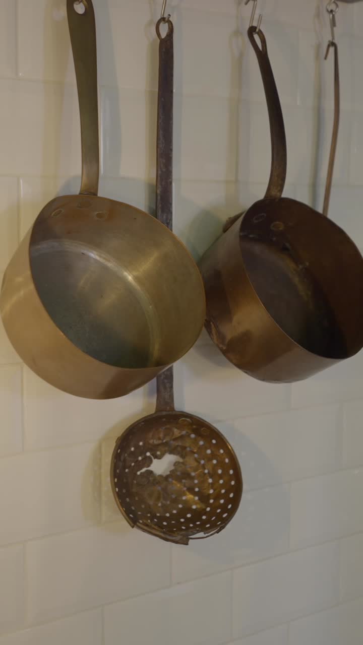 Various brass kitchenware and a light bulb hanging on white tiled walls