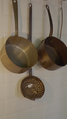 various brass kitchenware and a light bulb hanging on white tiled walls