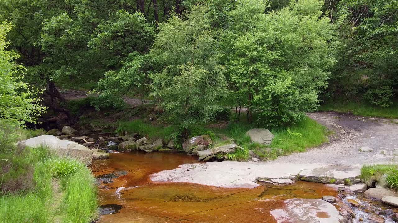 Drone footage of a meandering woodland stream in the Derbyshire Peak District with water flowing over small and large rocks