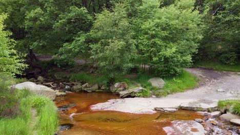 drone footage of a meandering woodland stream in the derbyshire peak district with water flowing over small and large rocks