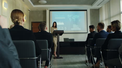 caucasian businesswoman talking on a podium in a conference room and showing some charts and graphics on the big screen