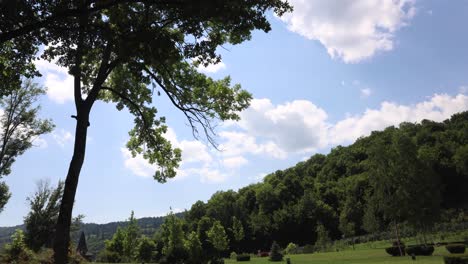 Wolken-Bilden-Sich-Am-Blauen-Himmel-Und-Grüne-Wälder,-Die-Sich-Tagsüber-In-Der-Sanften-Brise-Wiegen