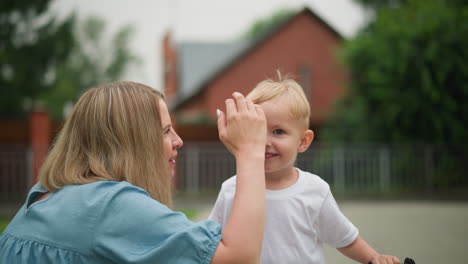 a joyful interaction between a mother and her young son outdoors, as she lovingly touches his head while they smile at each other