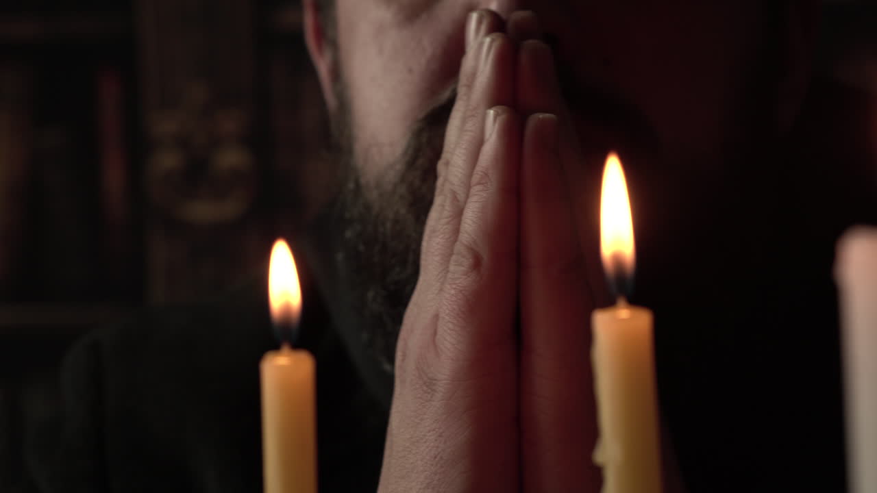 Priest With Folded Hands Praying to God in Front of Candles, Close Up