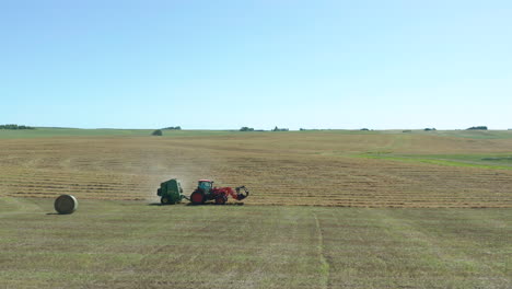 dolly in shot over agricultural land as tractor harvests bales of hay