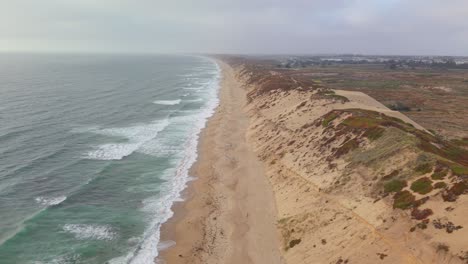 drone flies laterally over ocean waves, sandy beach, and dunes at fort ord dunes state park, marina, california