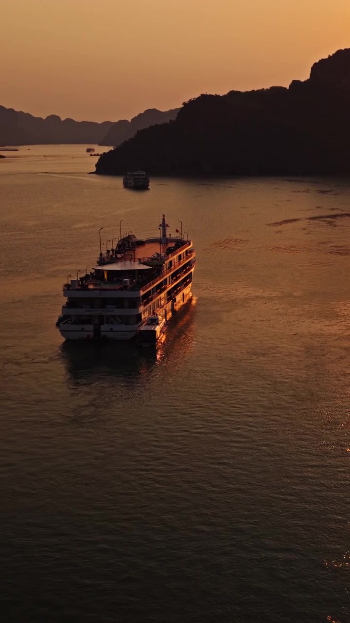 Lodret luftfoto af turbåd, der sejler i Ha Long-bugten ved gylden solnedgang, Vietnam.