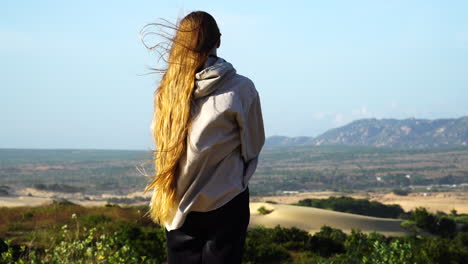 mujer por detrás con cabello largo rubio y camisa que sopla en el viento de pie en el mirador del paisaje escénico en vietnam