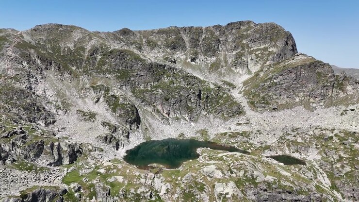 Ripide pareti rocciose si ergono sopra il lago Elenino nei monti Rila mentre un drone scivola dolcemente attraverso il circo alpino